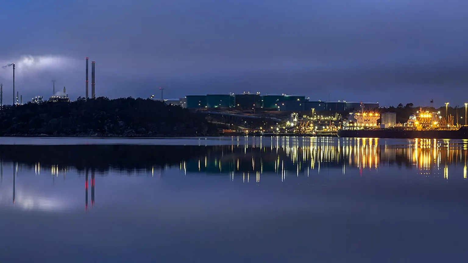 An oil refinery lit up at dusk across the water